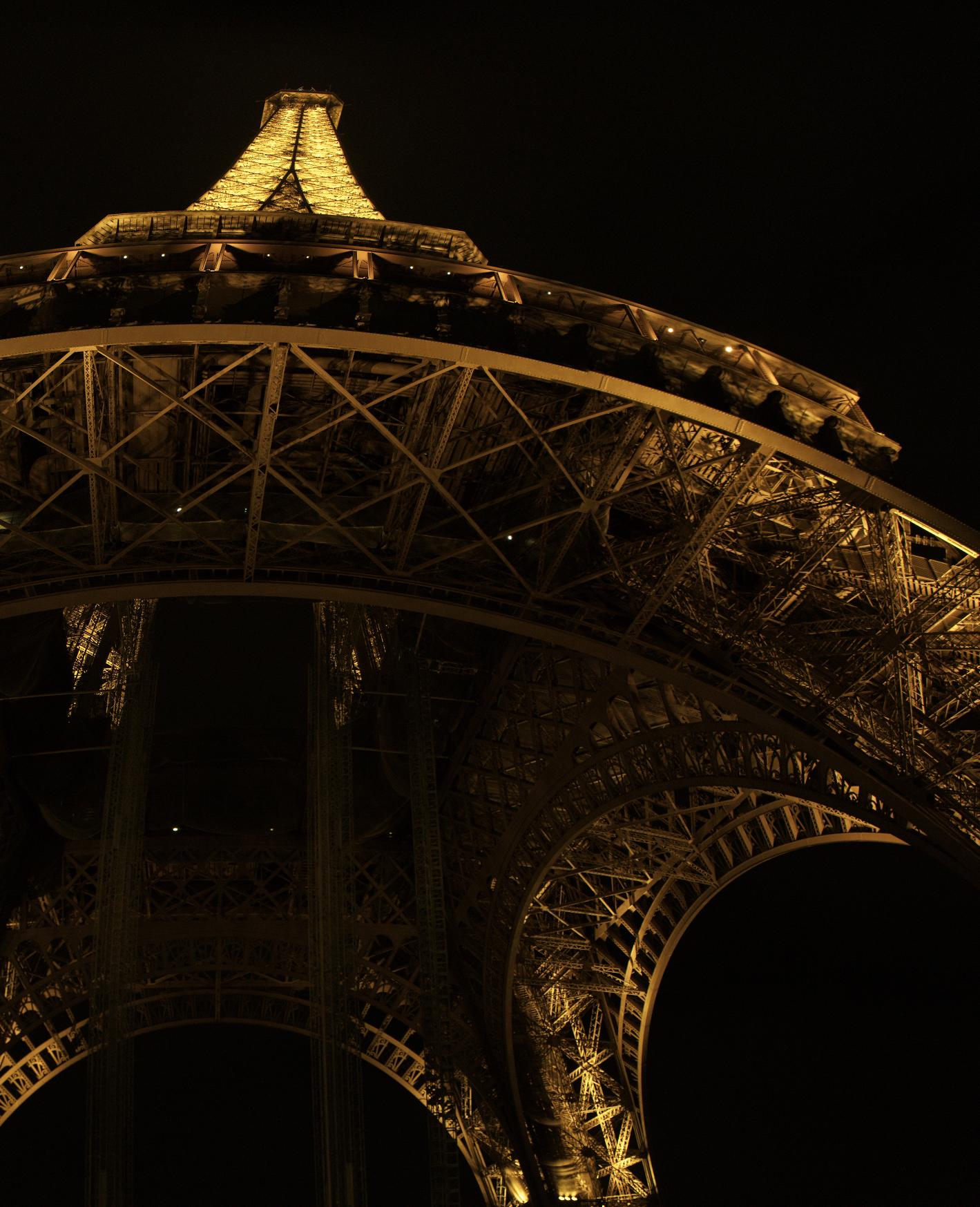 Vue nocturne rapprochée de la tour Eiffel éclairée depuis sa base, prise en contre-plongée.