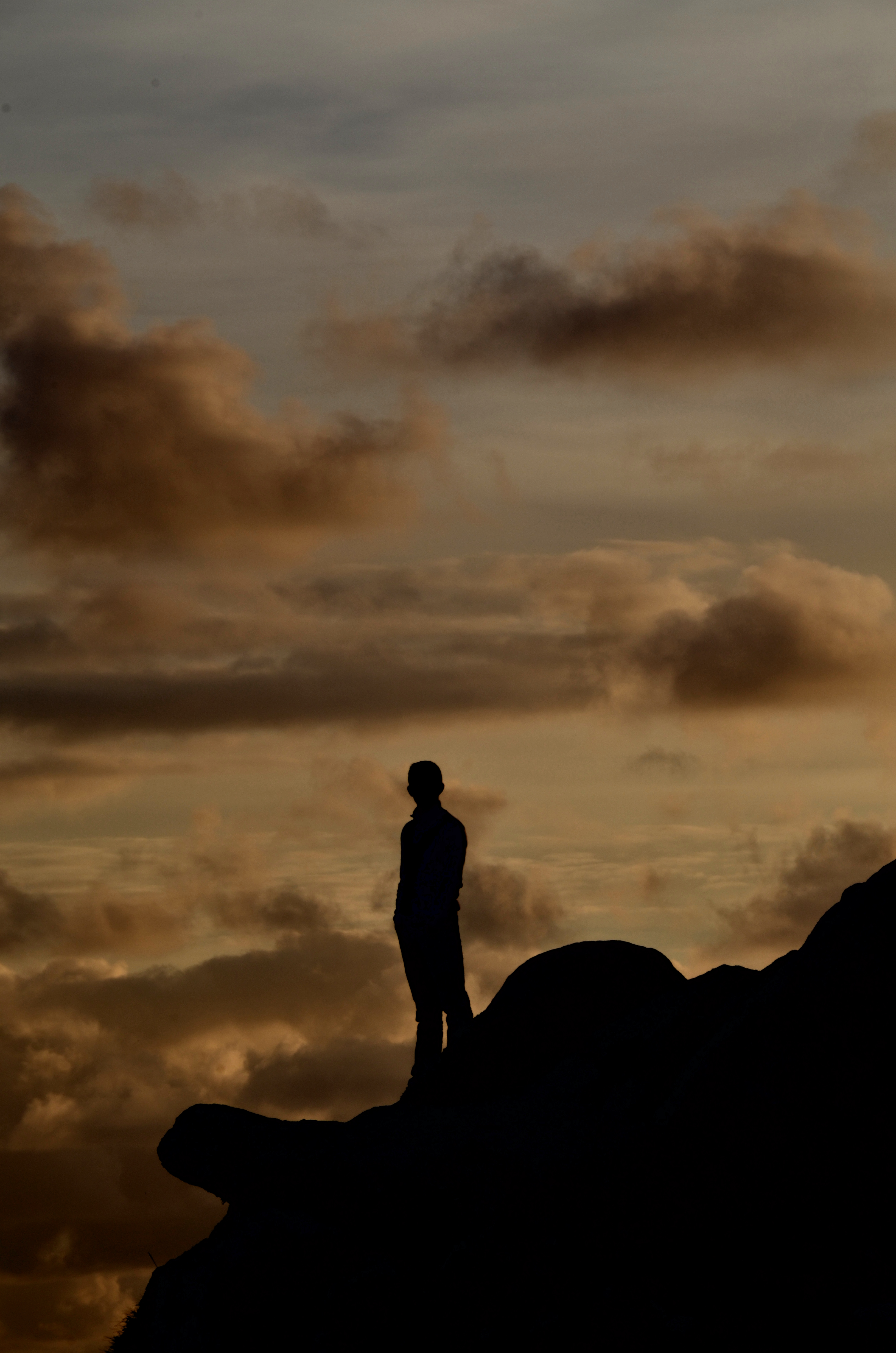 Silhouette d'une personne debout sur un rocher face à un ciel nuageux au crépuscule.
