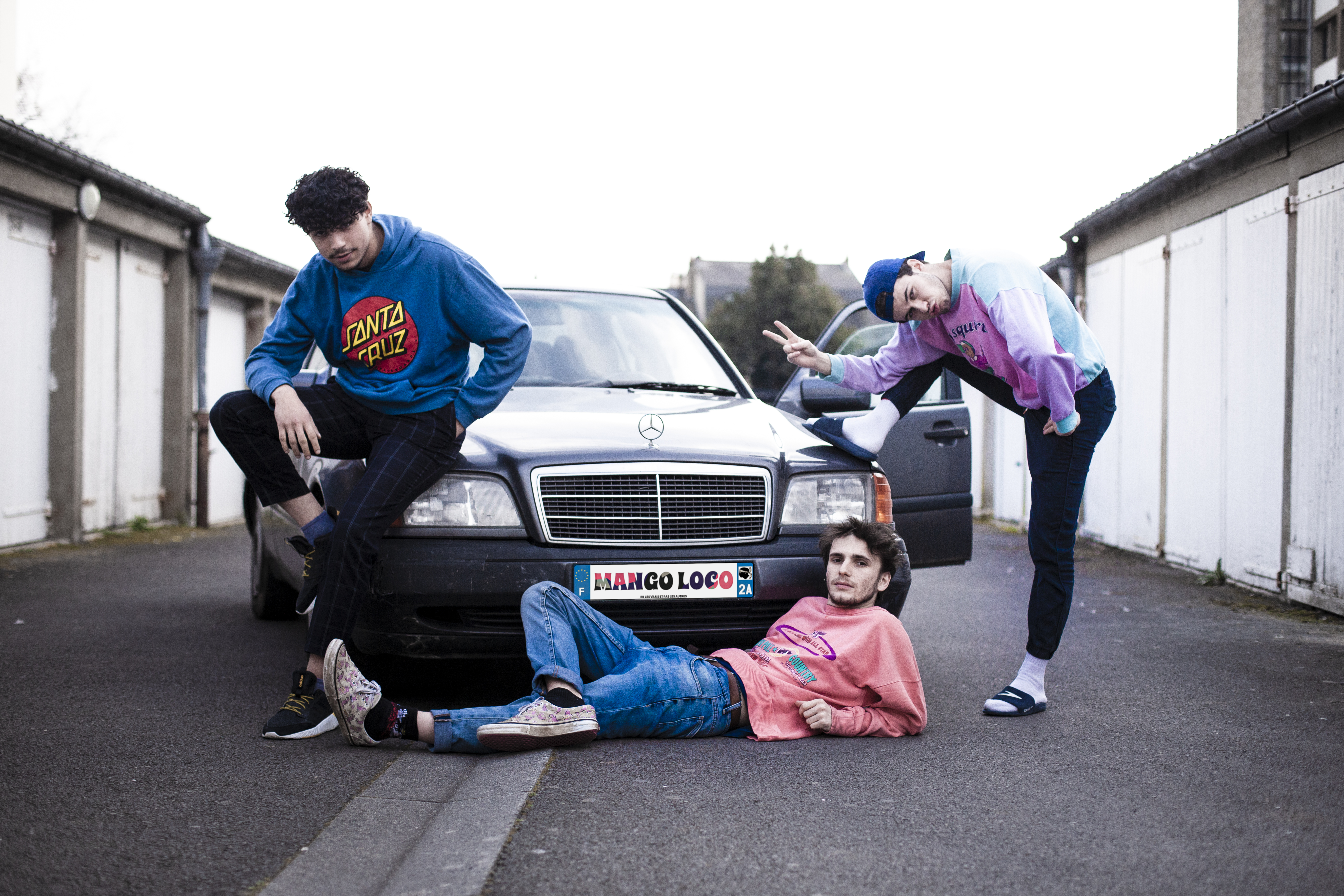 Trois jeunes posant avec une voiture, dans une ambiance décontractée et urbaine.