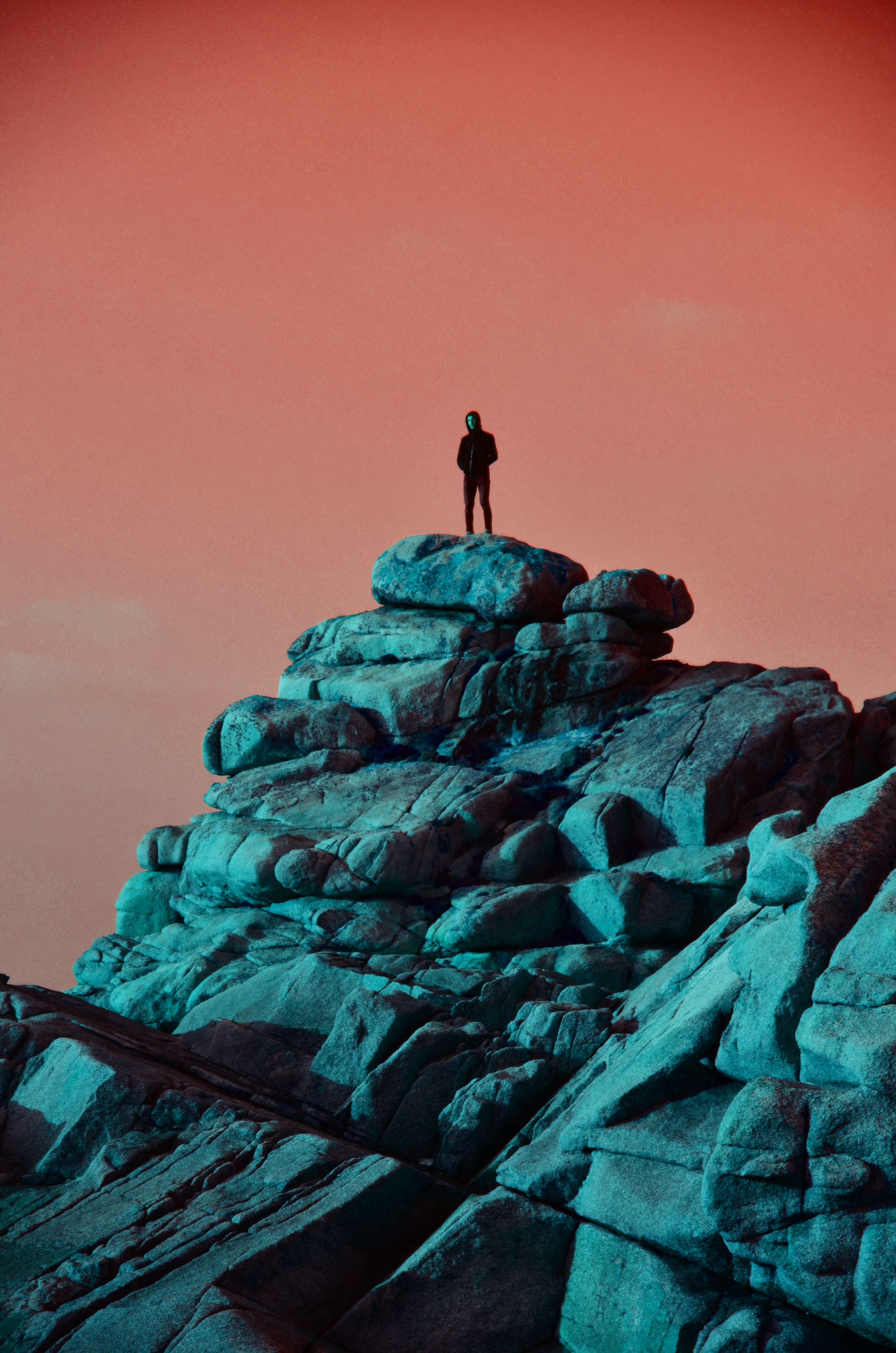 Personne debout sur un amas de rochers dans une ambiance surréaliste avec des teintes cyan et rose.