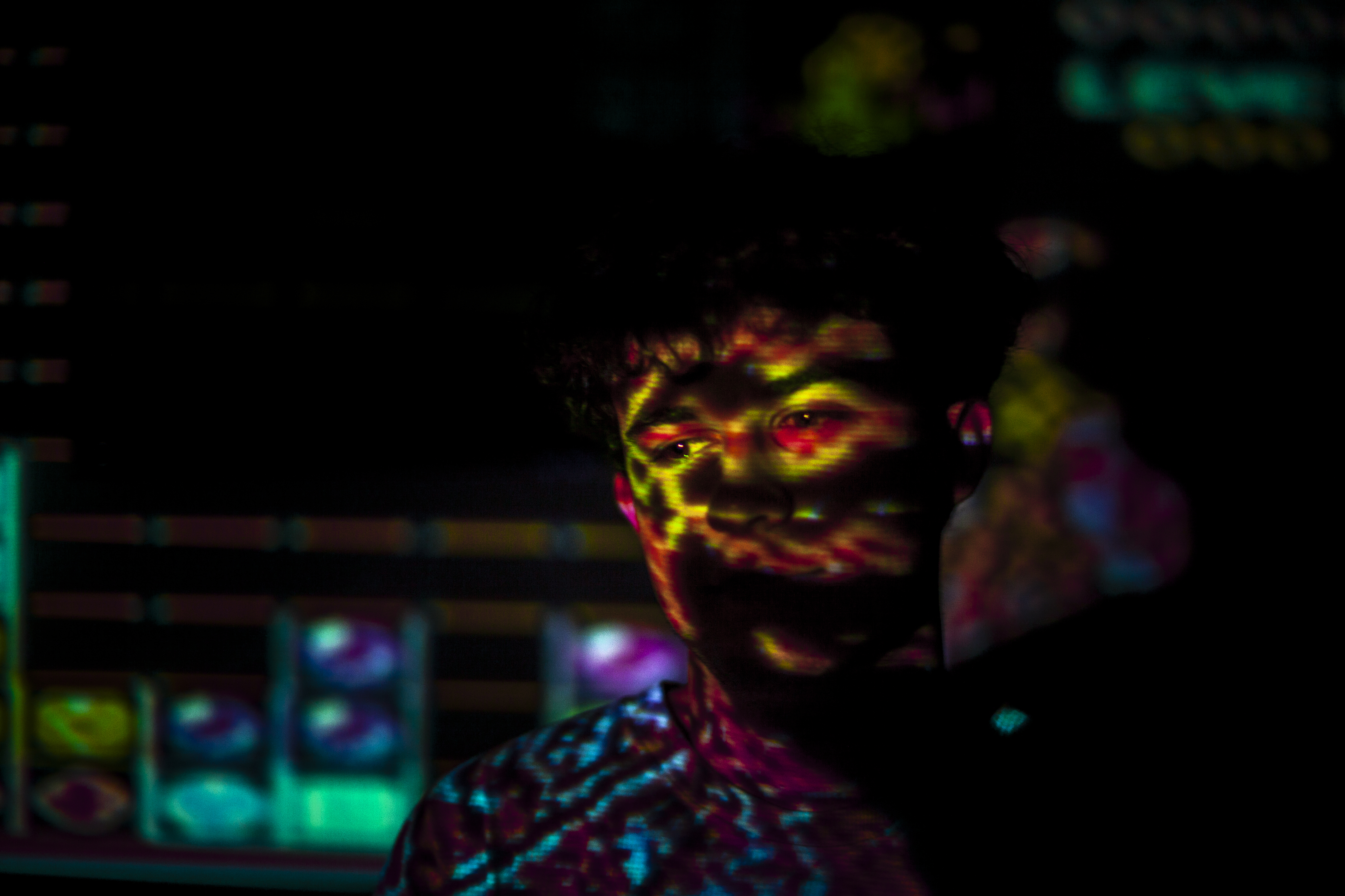 Visage d'une personne éclairé par la projection d'un jeu vidéo rétro, créant un effet visuel intense et coloré.