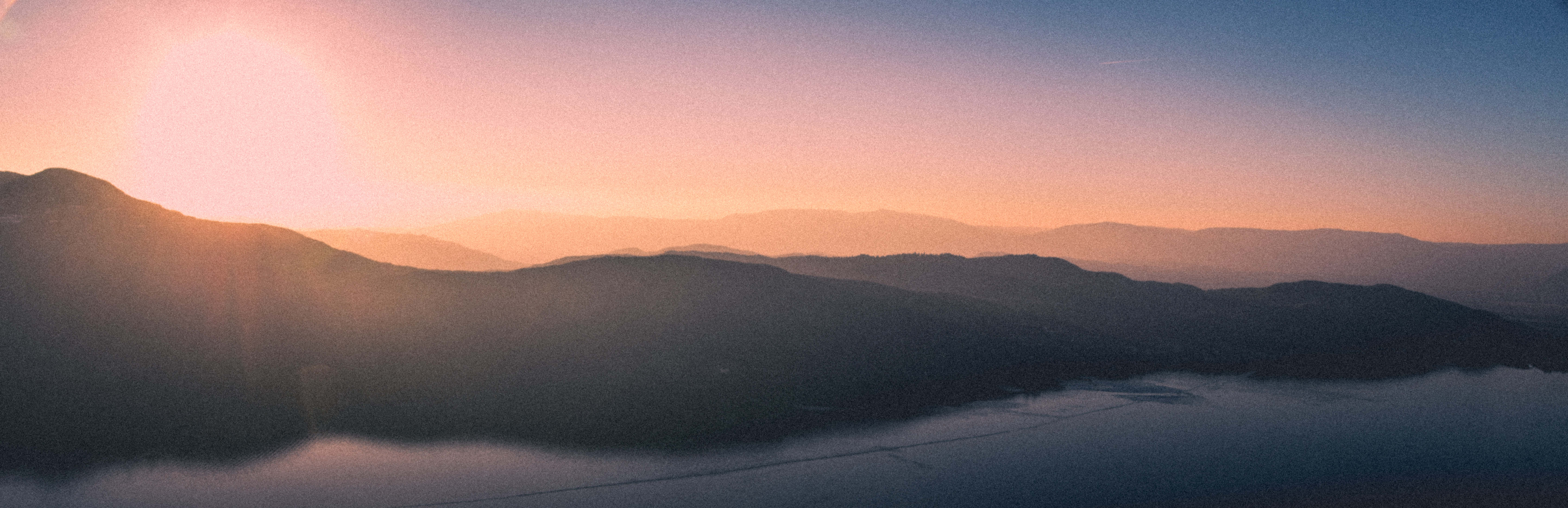 Paysage montagneux brumeux au lever du soleil avec des tons pastel et une lumière douce.