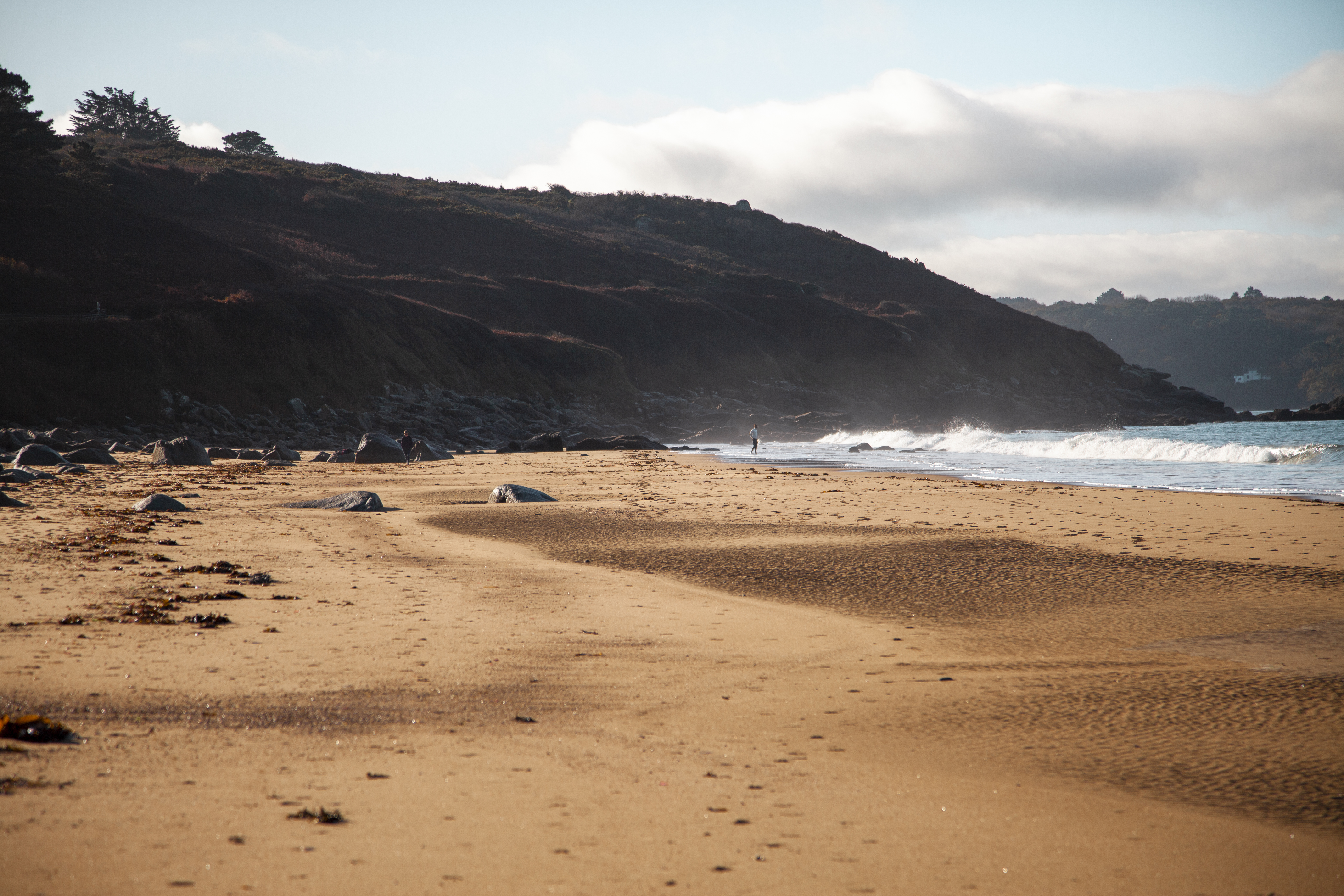 Plage de sable doré bordée de collines sombres avec des vagues déferlantes.