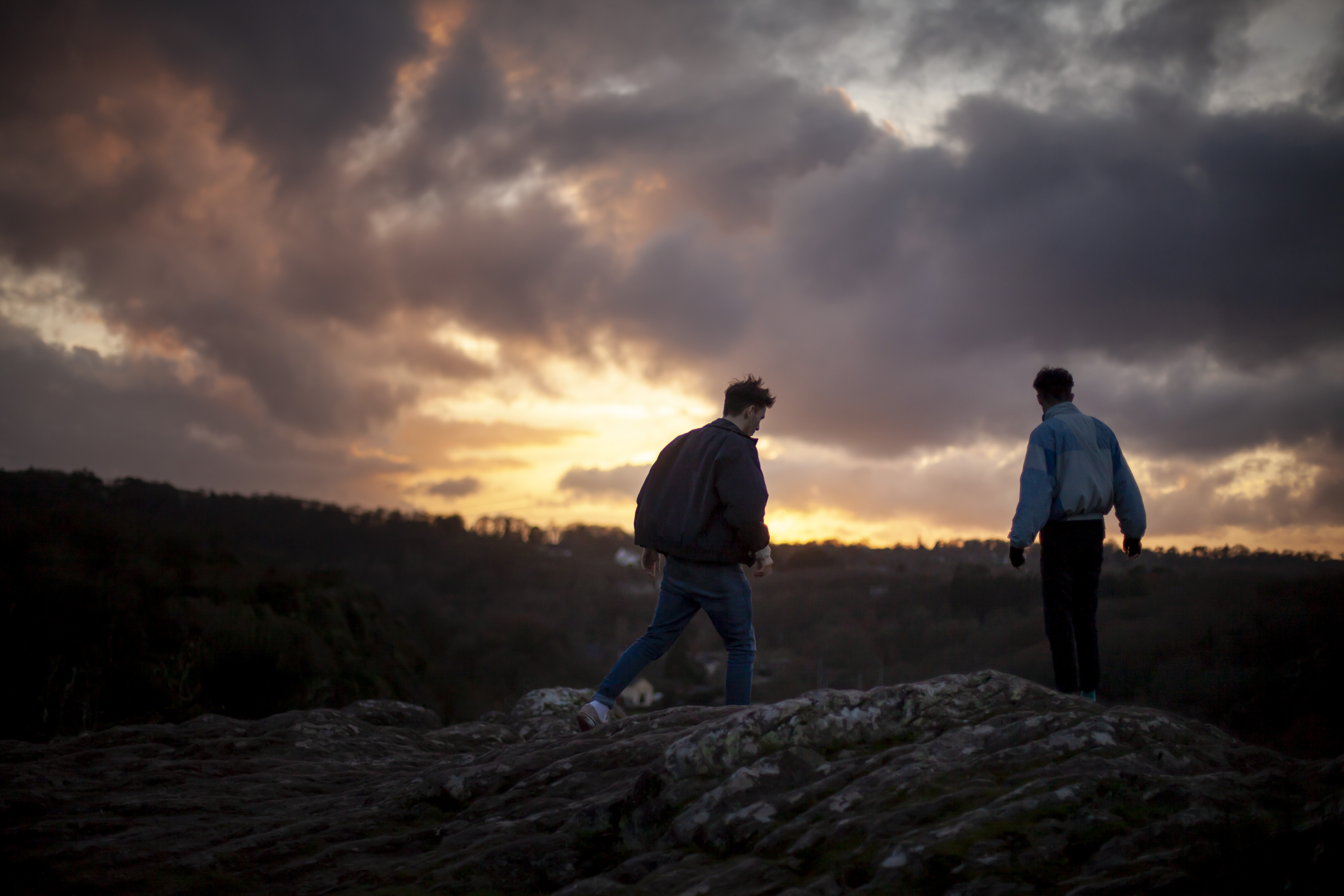 Deux personnes marchant sur un rocher au crépuscule sous un ciel dramatique.